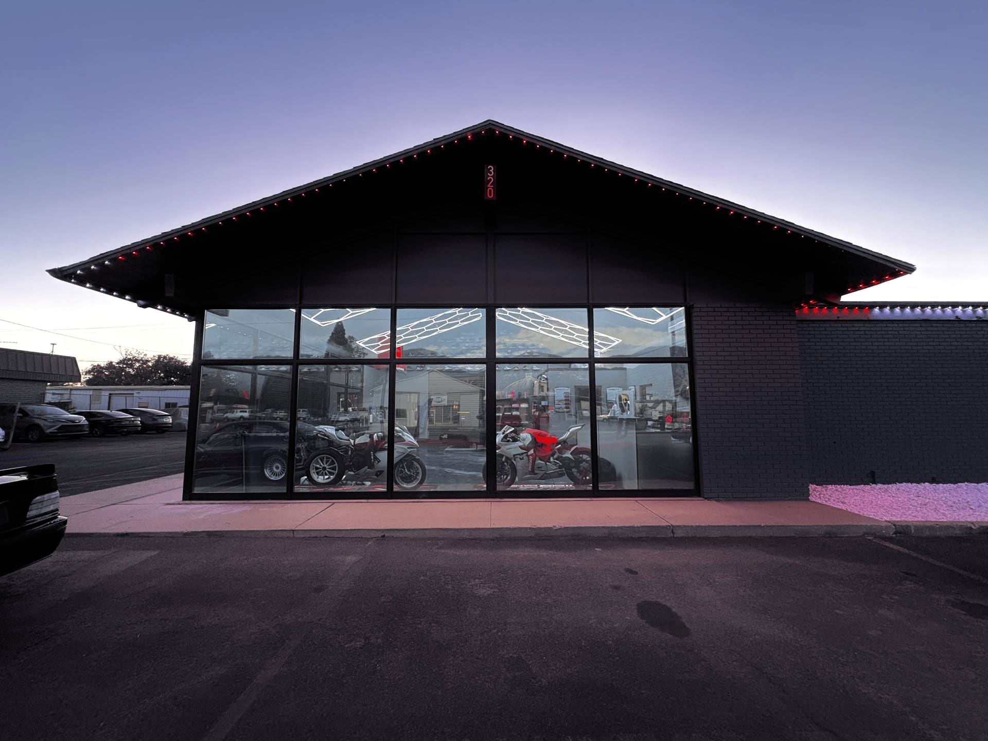Revolutionary Rides gable storefront at dusk with red roofline lighting and motorcycles displayed inside