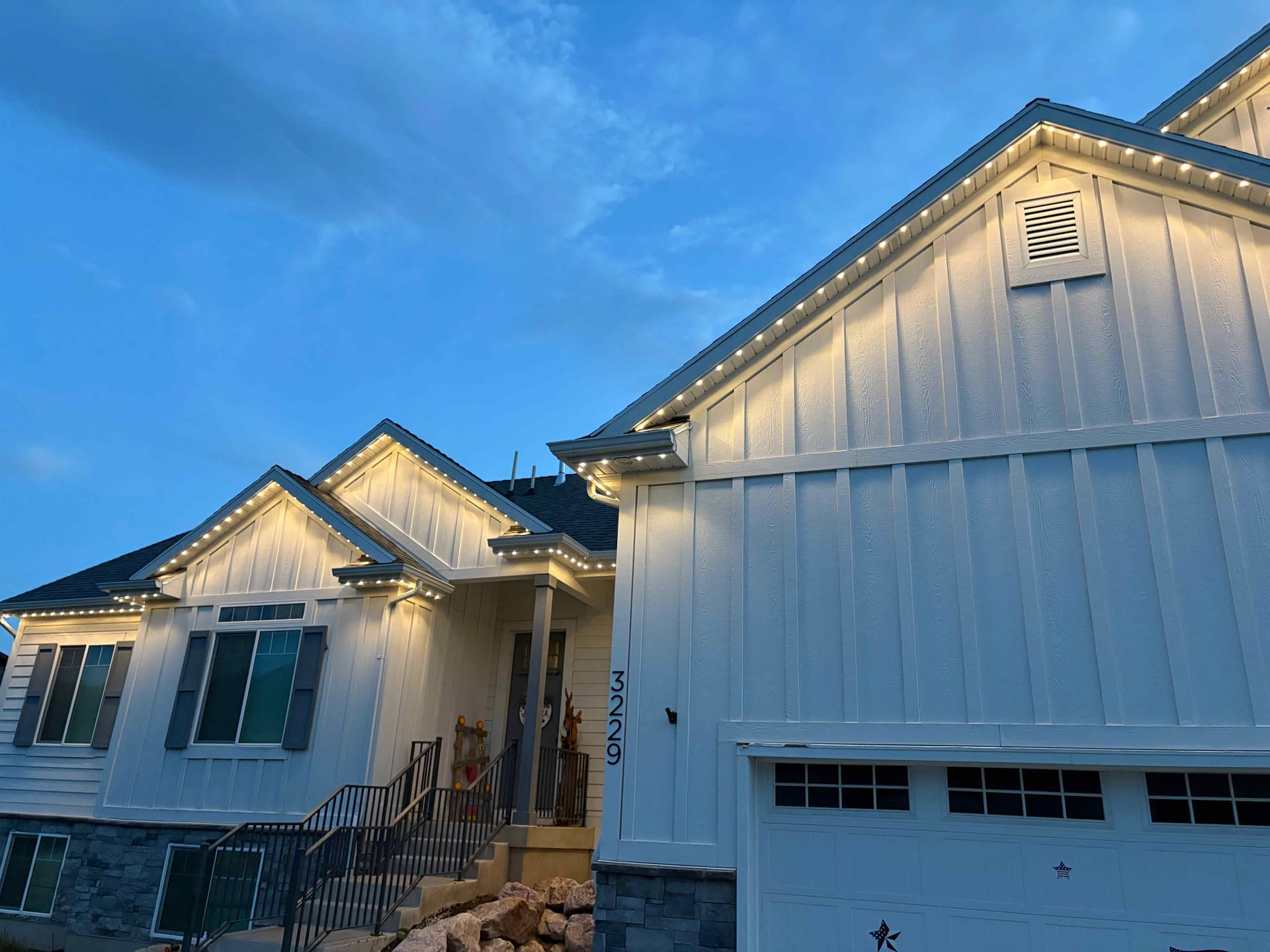 White board-and-batten home with warm white lighting under a blue dusk sky