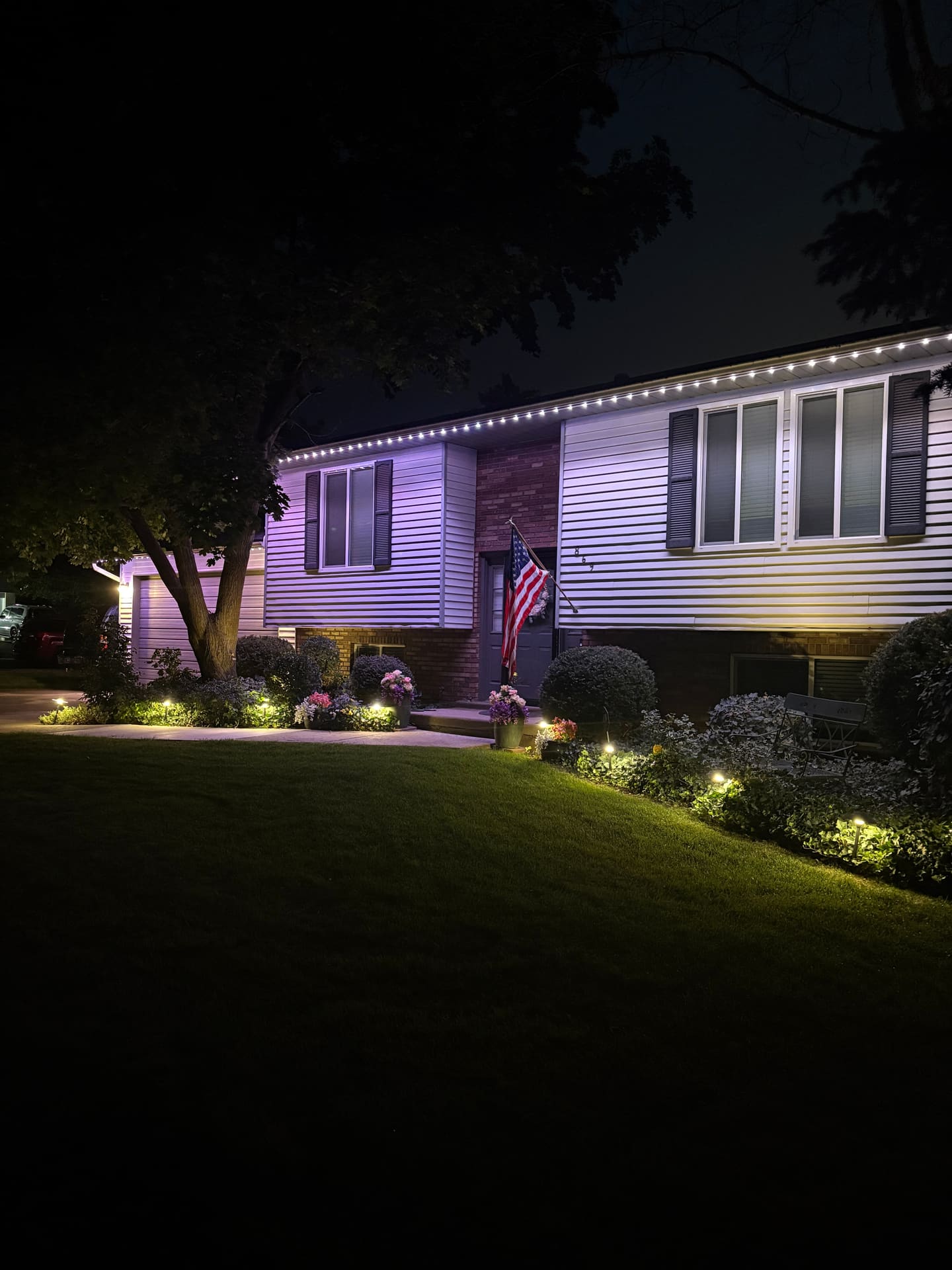 Split-level home with warm white eaves, a purple wall wash, and landscape spotlights